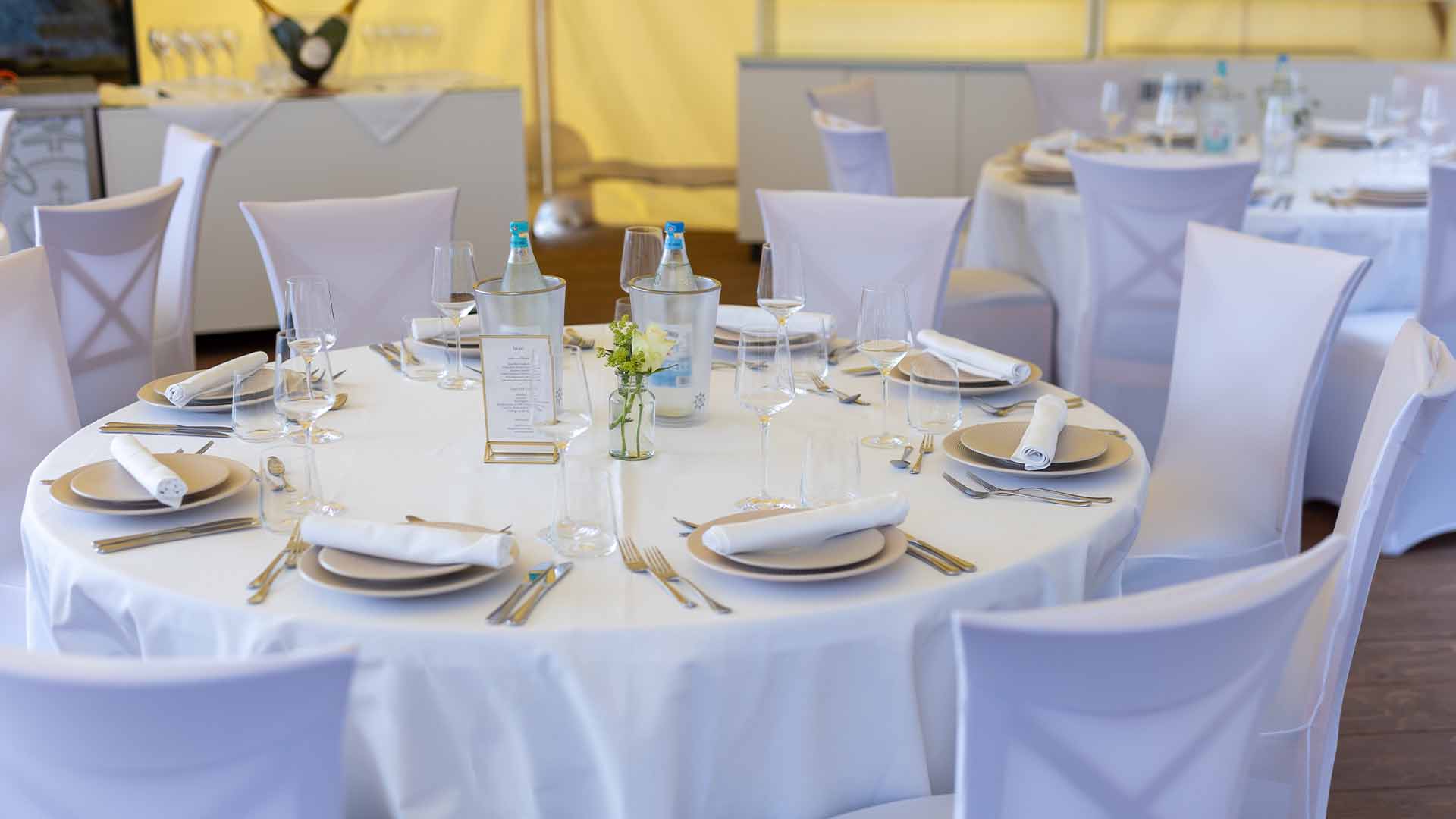Festlich eingedeckter Tisch mit Gläsern, Menükarte und Blumendekoration im Eventzelt