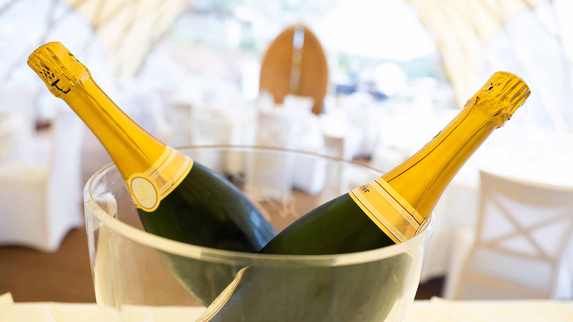 Zwei Champagnerflaschen im Kühler vor festlich gedeckten Tischen